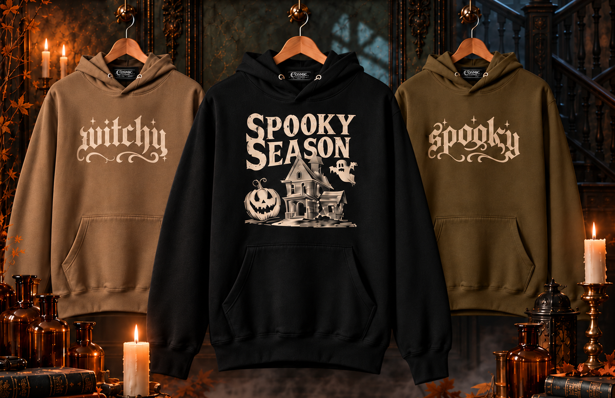 Three Cosmic Clothier hoodies — tan Witchy, black Spooky Season and olive spooky — hanging in a candlelit Victorian parlour with apothecary bottles and autumn leaves