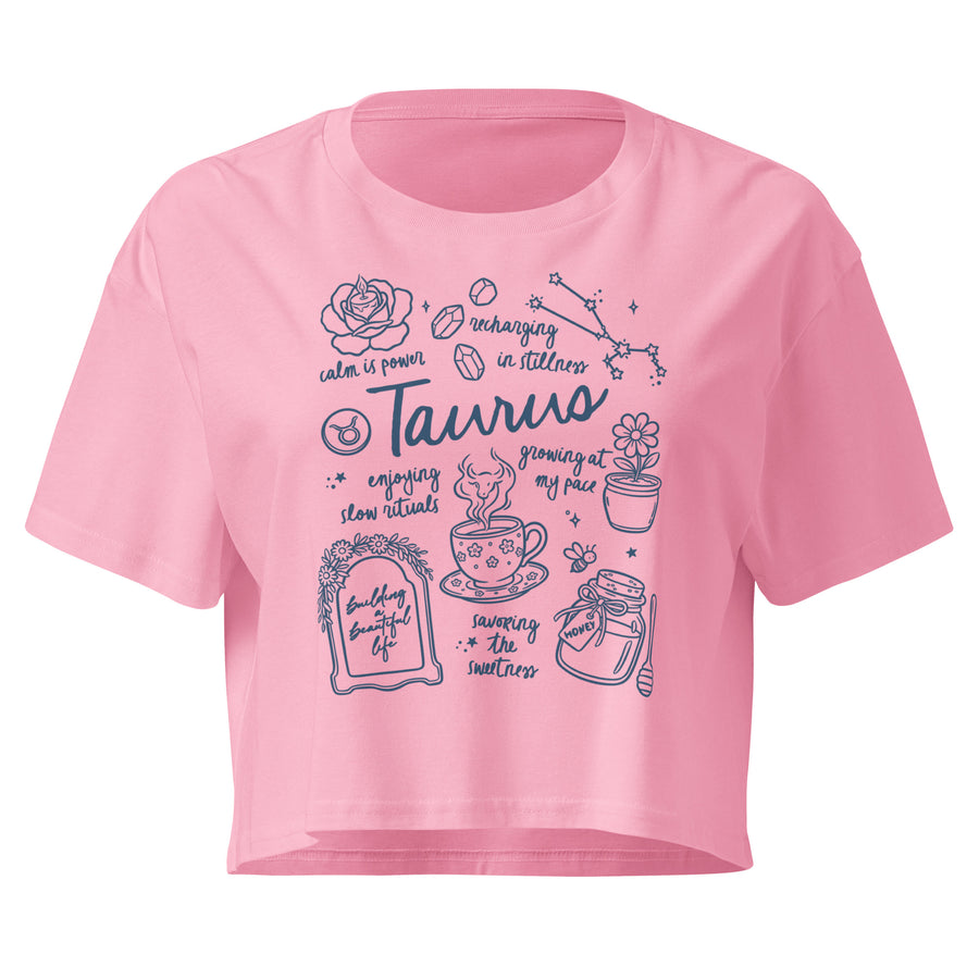 Bubblegum pink Taurus crop top with an indigo journal-style collage of zodiac traits and the bull glyph